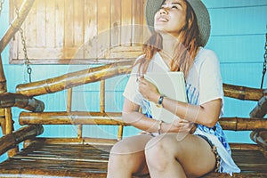 Asian women relax in the holiday. sit read a book on a wooden swing. Home Front porch. In Thailand