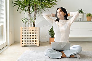 Asian woman relax  with laptop hands behind head  while sitting on the floor in morning sunlight at home