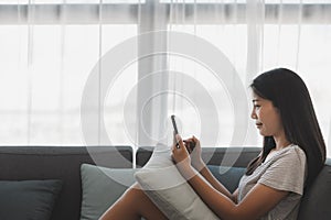 Asian woman relax and using mobile phone on sofa in living room at home