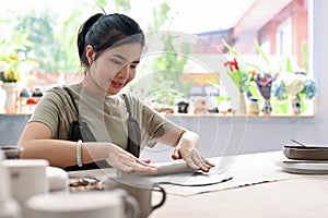 Asian woman relaxes rolling clay on worktable in the handcraft workshop. Moulding pottery