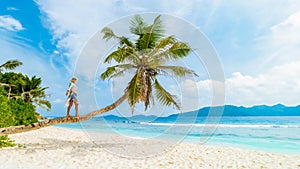 Asian woman relaxing at a coconut palm tree on a white tropical beach at La Digue Seychelles Islands