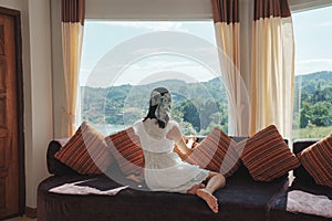 Asian woman relaxing and enjoying the tropical forest view on sofa at panorama room in bright day