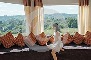 Asian woman relaxing and enjoying the tropical forest view on sofa at panorama room in bright day