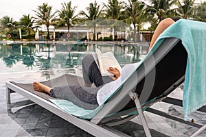 Asian woman relaxing and reading book at the swimming pool
