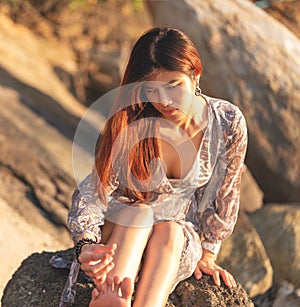 Asian woman is relaxing on a rock on a Sunny Beach for Summer vacation relaxation and hapiness concept