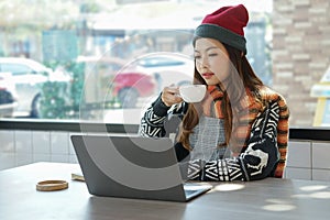 Asian woman relaxing by sip a hot drink while offsite working with laptop in the winter
