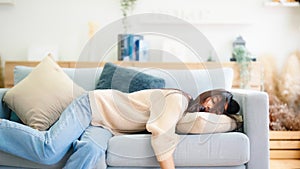 Asian woman resting at home on couch, feeling exhausted after work