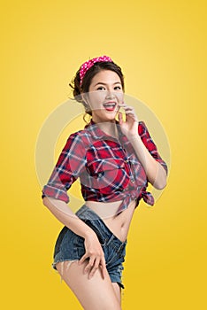 Asian woman retro portrait with pin-up make-up and hairstyle posing over yellow background.