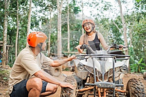 asian woman riding the atv while the asian man checking on it