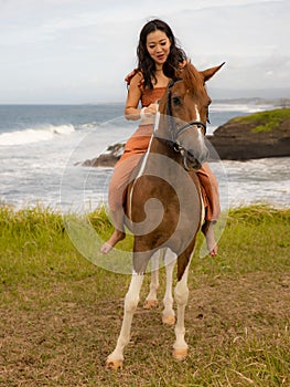 Asian woman riding horse near the ocean. Outdoor activities. Traveling concept. Vertical layout. Bali