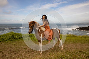 Asian woman riding horse near the ocean. Outdoor activities. Wcuddling her horse. Traveling concept. Copy space. Bali