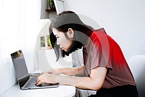 Asian woman's back and shoulder pain with incorrect posture while working on a computer