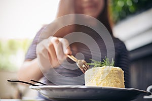 An Asian woman`s hand cutting cheese cake with fork