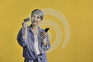 Asian woman 50s holding smartphone and credit card shopping online isolated on colour background