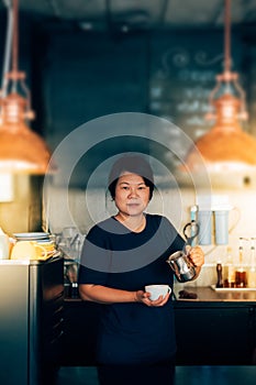 Asian woman barista pouring latte in coffee shop