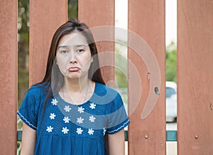 Asian woman with sad face emotion on blurred wooden fence background