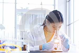 Asian woman scientist looking at microscope working test chemical in laboratory