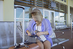 An asian woman searches her bag for her wallet or passport while outside the arrival area of an airport. Possibly forgotten at the