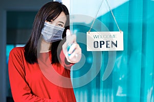 Asian woman shop owner smiling hanging label `Welcom we are open` and showing thump up photo