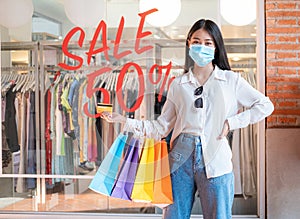 Asian woman shopaholic wearing face mask with many colorful shopping bags and holding credit card