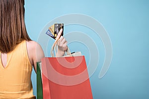 Asian woman with shopping bags showing credit card in hands.