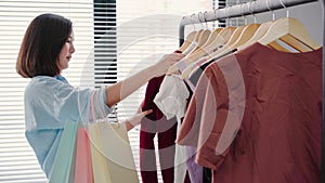 Asian woman shopping clothes. Shopper looking at clothing on the rail indoors in clothing store. Beautiful happy smiling asian