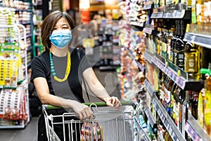 Asian woman shopping groceries in supermarket with protective face mask as new normal requirement