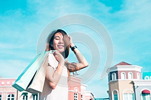 Asian woman shopping an outdoor flea market with a background of pastel buildings.