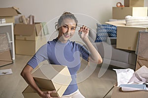 Asian woman showing keys and holding cardboard boxes in new house, smiling and looking at camera