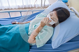 Asian woman is sick has a high fever, sneezing, is recuperating in the patient`s dress lay on the patient bed in the hospital wit photo