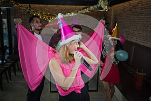 Asian woman singer in santa claus hat with a microphone singing and dancing in Christmas party and friend in restaurant.