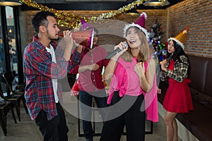 Asian woman singer in santa claus hat with a microphone singing and dancing in Christmas party and friend in restaurant.