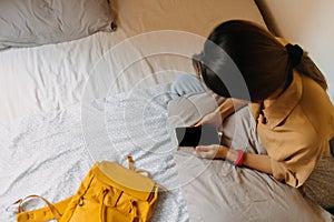 Asian woman sit on the bed in a small bedroom of budget hotel.