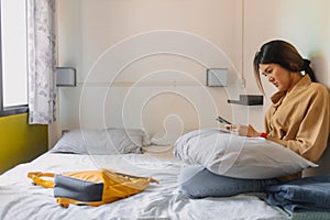 Asian woman sit on the bed in a small bedroom of budget hotel.