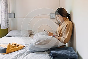 Asian woman sit on the bed in a small bedroom of budget hotel.