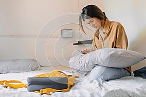 Asian woman sit on the bed in a small bedroom of budget hotel.