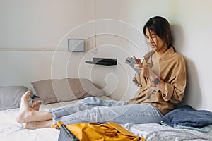 Asian woman sit on the bed in a small bedroom of budget hotel.