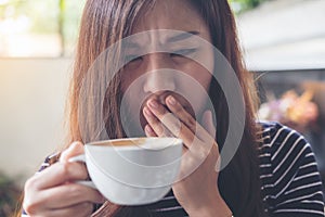 Asian woman sit with chin resting on her hands and closing her eyes smelling hot coffee on wooden table with feeling good in cafe