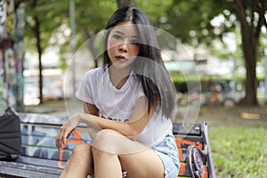 Asian woman sits on a public bench in a park