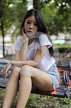 Asian woman sits on a public bench in a park