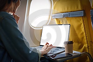 An Asian woman sits in a window seat in Economy Class using a white screen laptop computer that can use text or