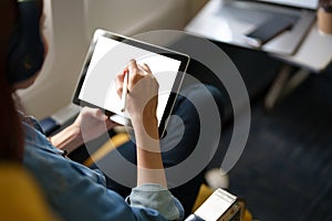 An Asian woman sits in a window seat in Economy Class using a white screen tablet that can use text or advertising while