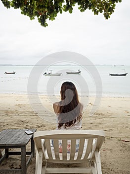 Asian woman sitting on beach chair looking away to sea view. Samed, Thailand.