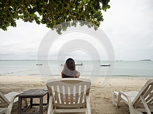 Asian woman sitting on beach chair looking away to sea view. Samed, Thailand.