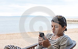 Asian woman sitting at the beach closely looking at her cell phone reading and looking focused