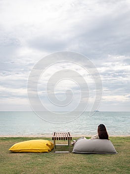 Asian woman sitting on bean bag in garden near the beach. female looking out the sea view. rear view.