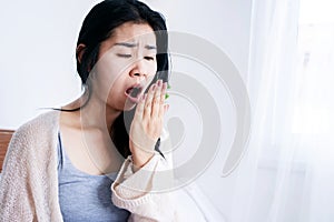 Asian woman sitting in bed open mouth checking her bad breath smell after wake up in the morning