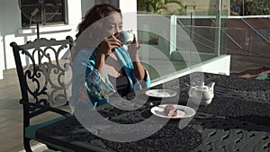 Asian woman is sitting on black ironed table and drinking tea on a terrace, enjoy morning fresh air with view