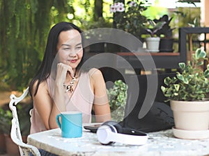 Asian woman in sitting with blue coffee cup on table in her home garden, using computer notebook,does`n believe from what she`s