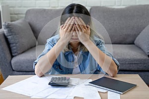 Asian woman sitting covering face with hands with many bills on table at home. she feels stressed. Debt or bankruptcy concept